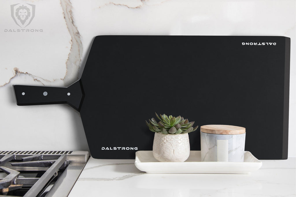 Large black cutting board with handle rests against a white kitchen wall