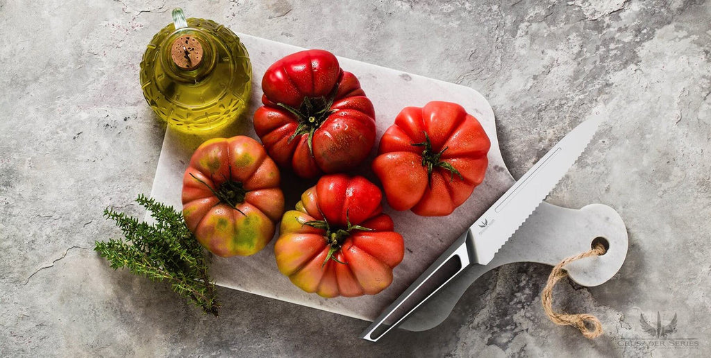 A serrated knife on a cutting board next to four red peppers