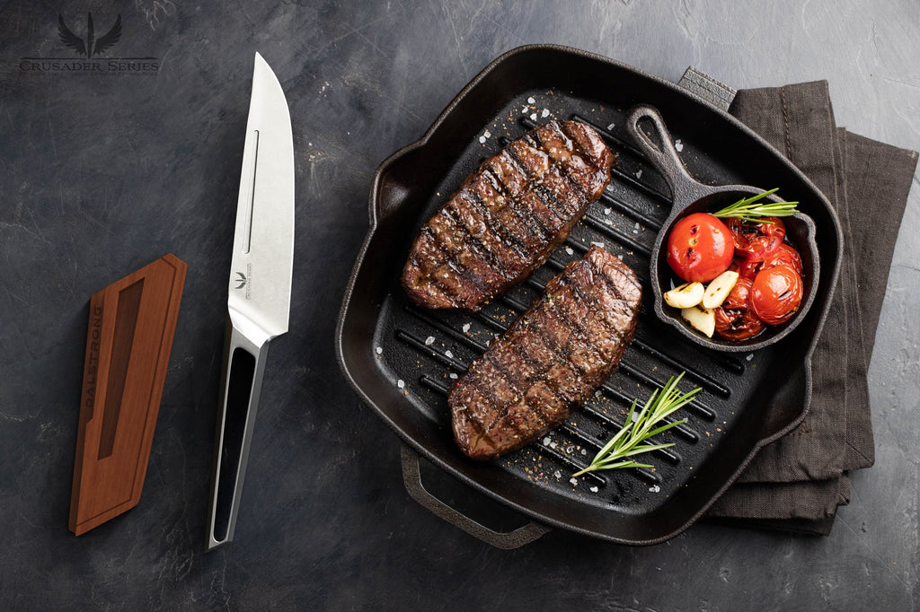 Stainless Steel Knife beside a grill pan thats cooking two steaks and some tomatoes
