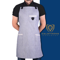 Man standing with his hands behind his back displaying “The Gandalf” grey denim apron with a white and blue background and proformapeakmarketing logo