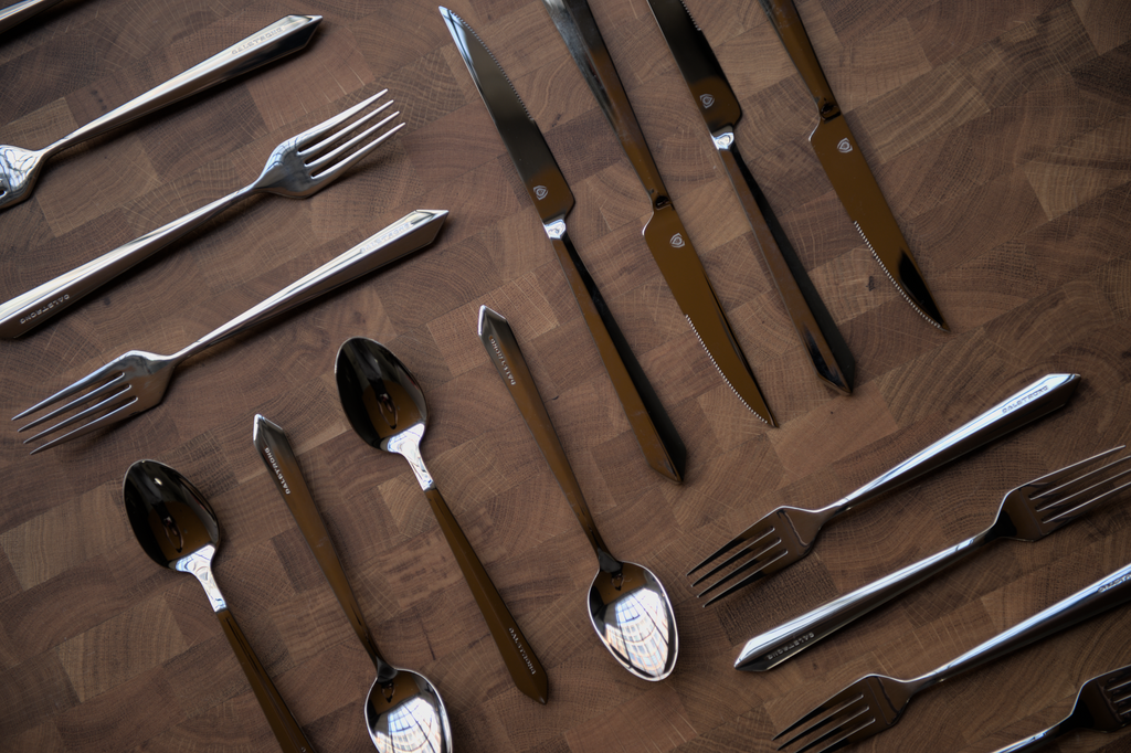 A flat-lay photo of the proformapeakmarketing 20-Piece Flatware Set on a wooden cutting board.