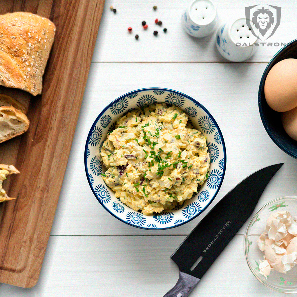 A bowl of egg salad with a proformapeakmarketing Delta Wolf Series knife on the side and slices of bread on a wooden cutting board.