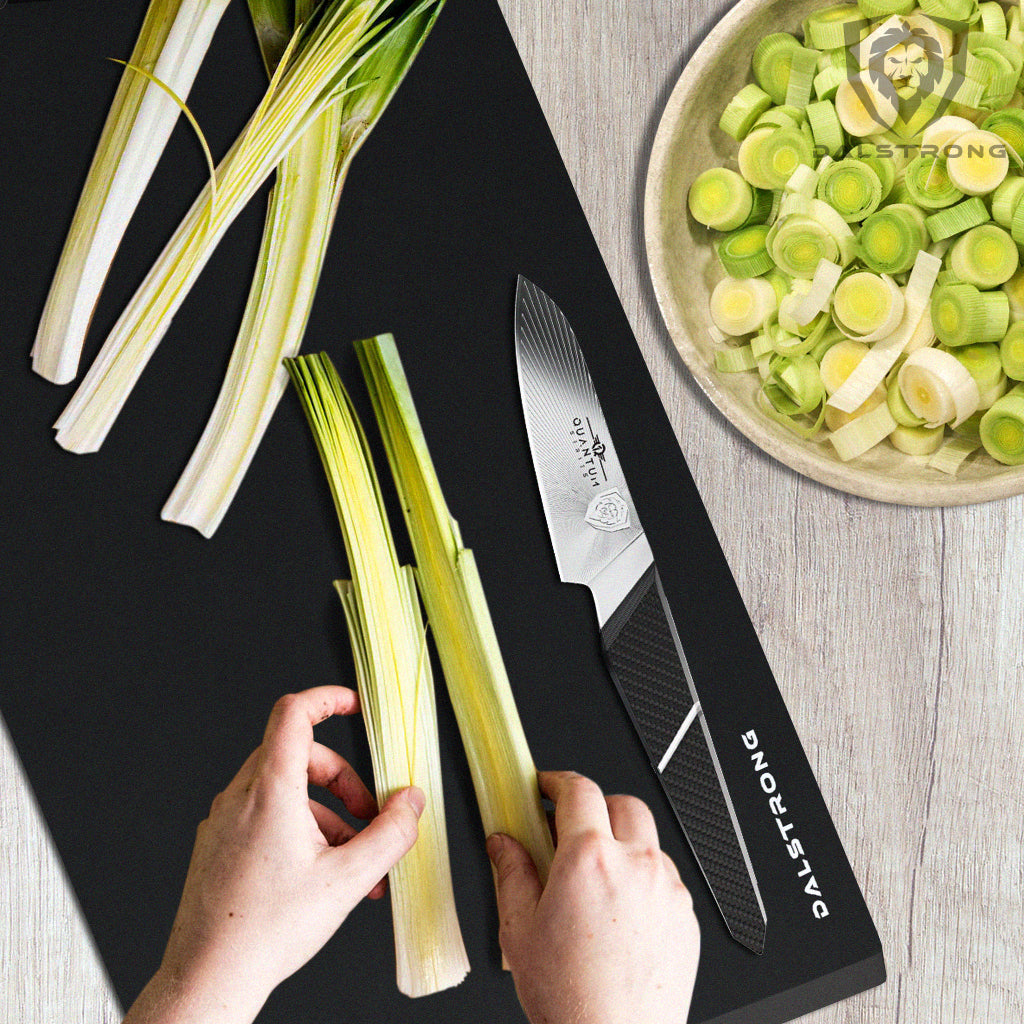 paring knife cutting a leek down the middle on a black cutting board