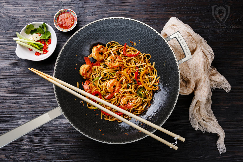 A black interior wok with cooked noodles and vegetables and chopsticks resting on its edge