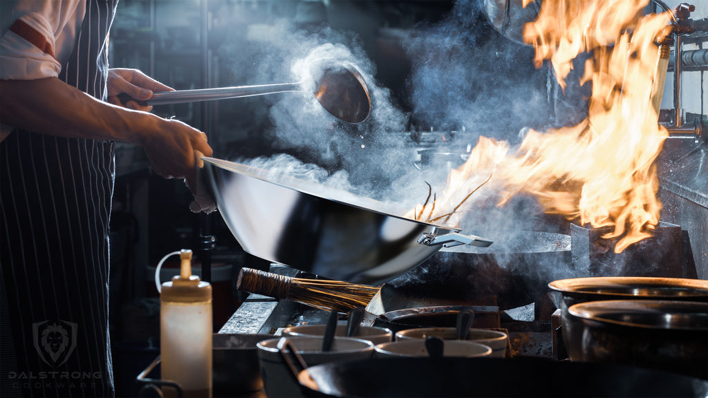 A chef using a smoking wok with flames emerging in a dark kitchen