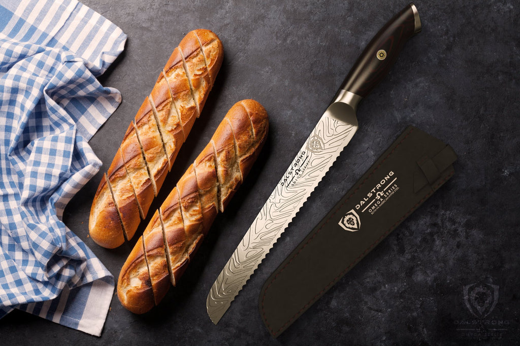 Large serrated bread knife laying beside two uncut loafs of bread on a black counter