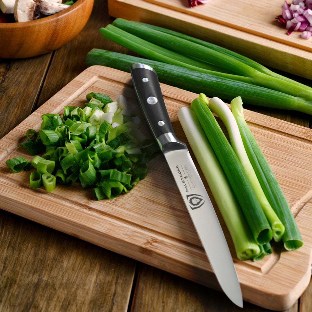 Sharp kitchen knife on a wooden cutting board next to chopped green onions