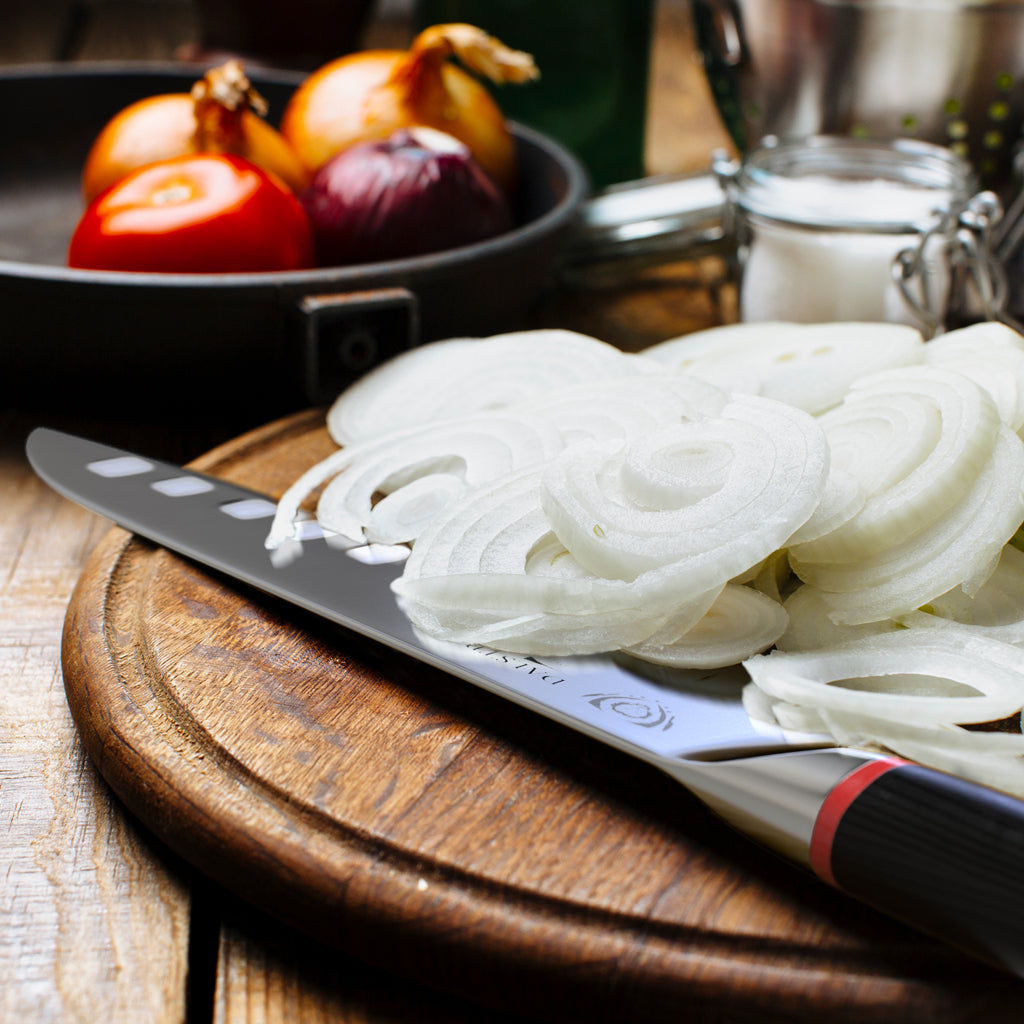Sliced white onions covering a portion of a Japanese kitchen knife on a wooden cutting board