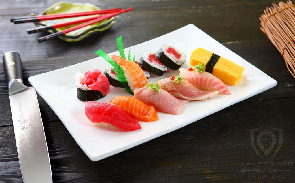 An assortment of sushi on a white plate next to a yanagiba knife