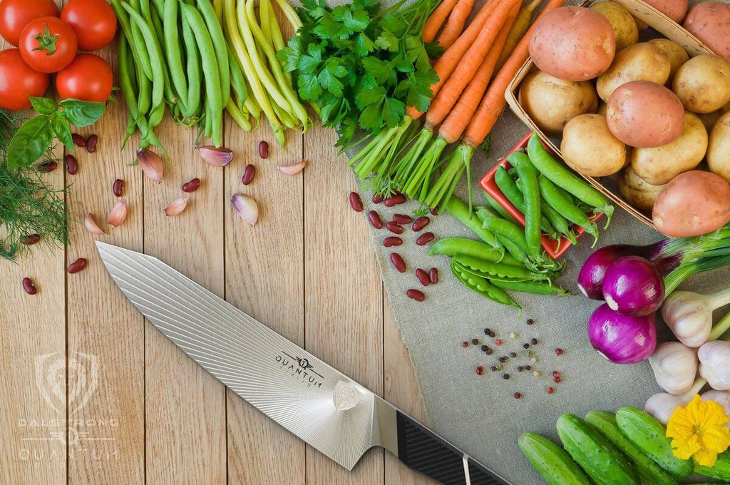 A razor sharp chef knife surrounded by a variety of vegetables on a wooden surface