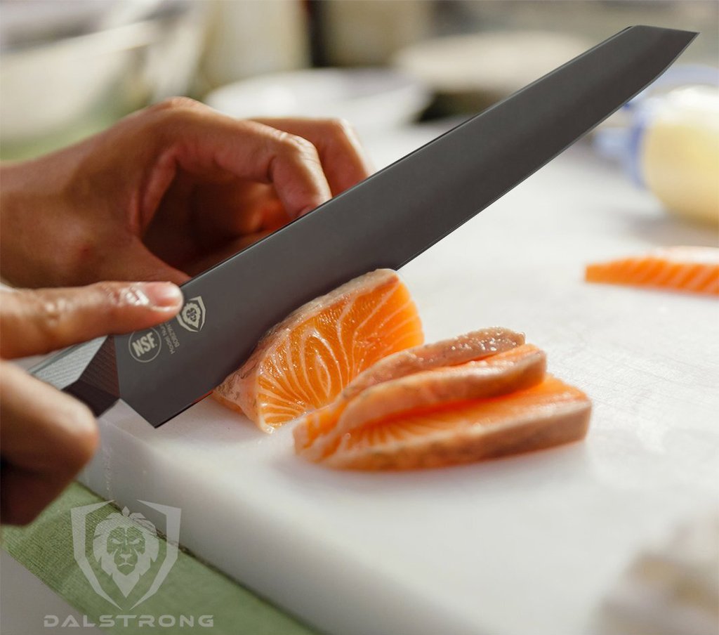 A black yanagiba knife slicing through raw fish on a white surface