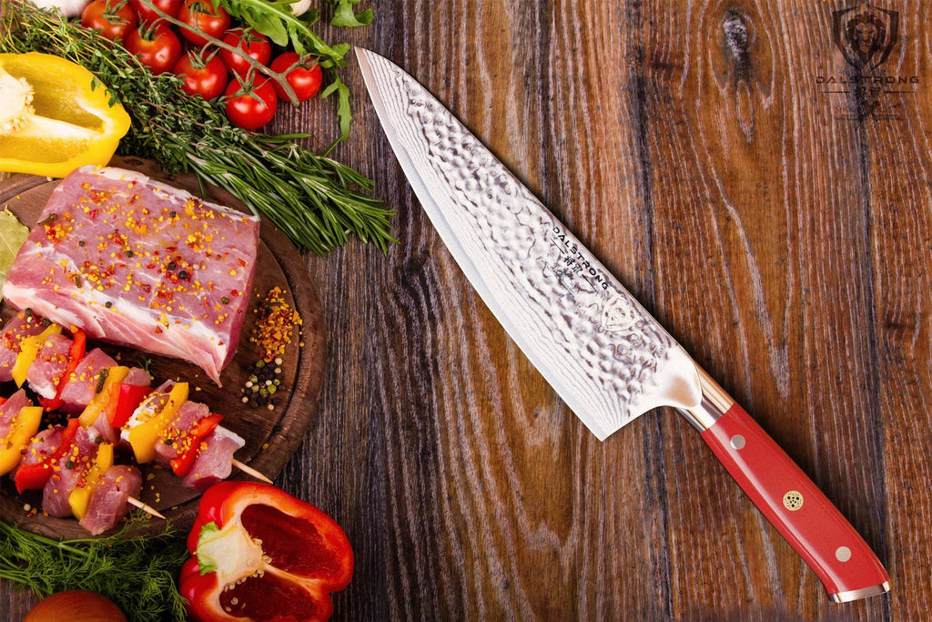 Sharp kitchen knife with red handle next to an assortment of vegetables and uncooked chicken on a wooden table