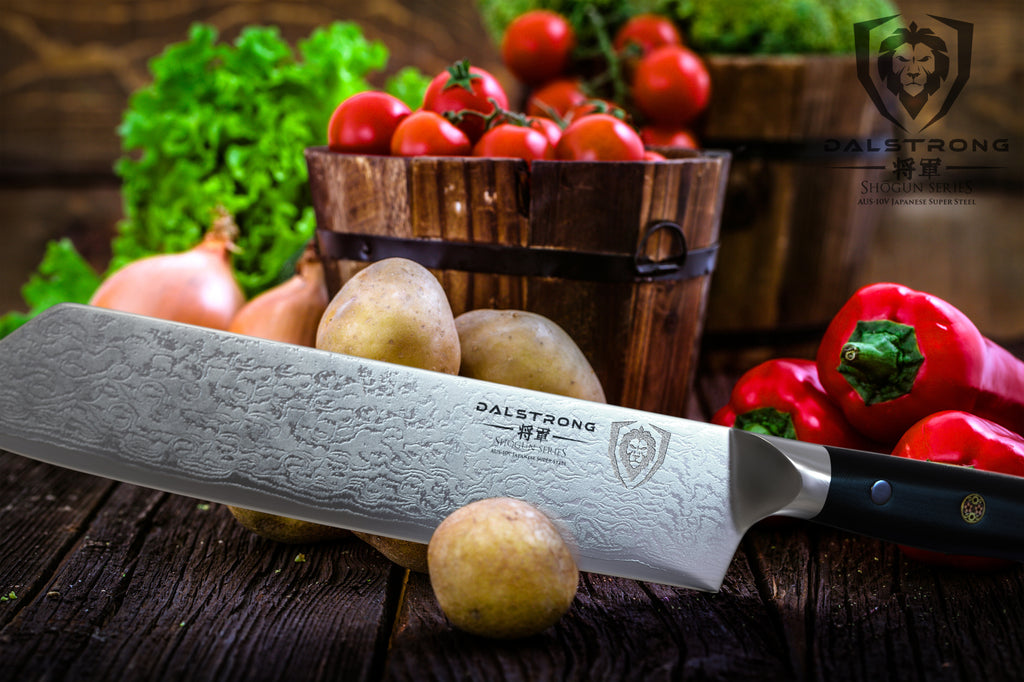 Kiritsuke knife with damascus steel chopping a small potato with more produce in the background