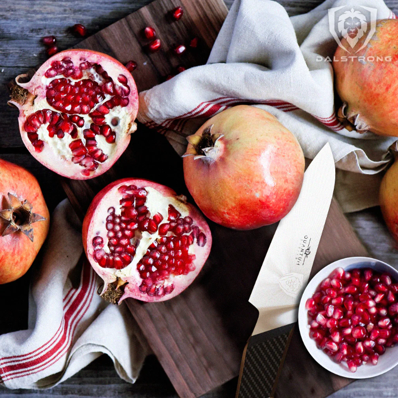 A photo of a pomegranate sliced in half with the 4'' Paring Knife Quantum Series proformapeakmarketing on top of a wooden board