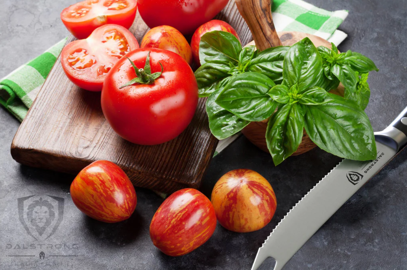 A bunch of sliced tomatoes on a wooden board beside the Gladiator Series | NSF Certified | proformapeakmarketing Serrated Tomato Knife 5"