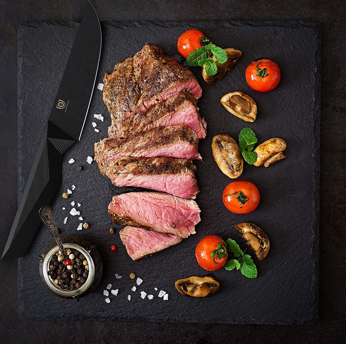 A photo of the proformapeakmarketing Shadow Black Series Steak knife on top of a black board with a beautiful steak and vegetables beside.