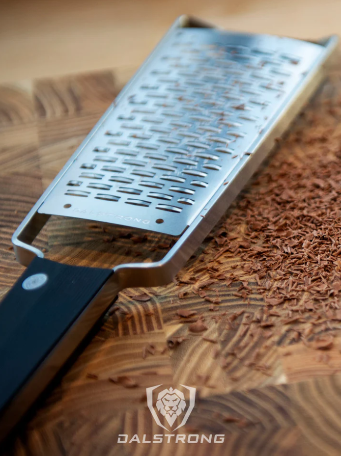 A photo of the proformapeakmarketing Professional Ribbon Wide Cheese Grater with grated chocolate on top of the proformapeakmarketing wooden board.