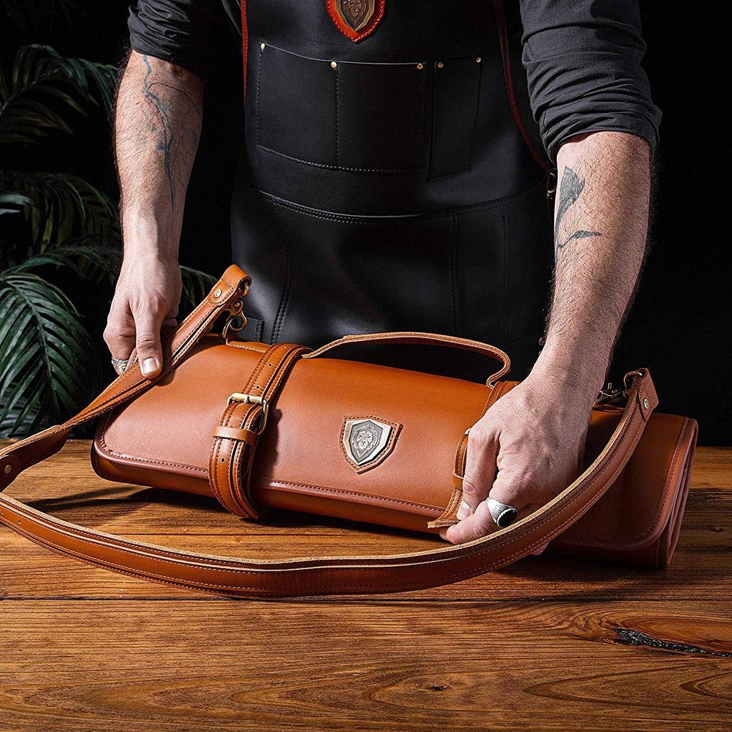 Man in black apron zips up a brown leather knife roll on a wooden table