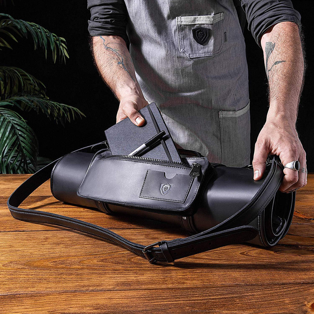 A chef places a leather book into his black leather knife roll on a wooden table