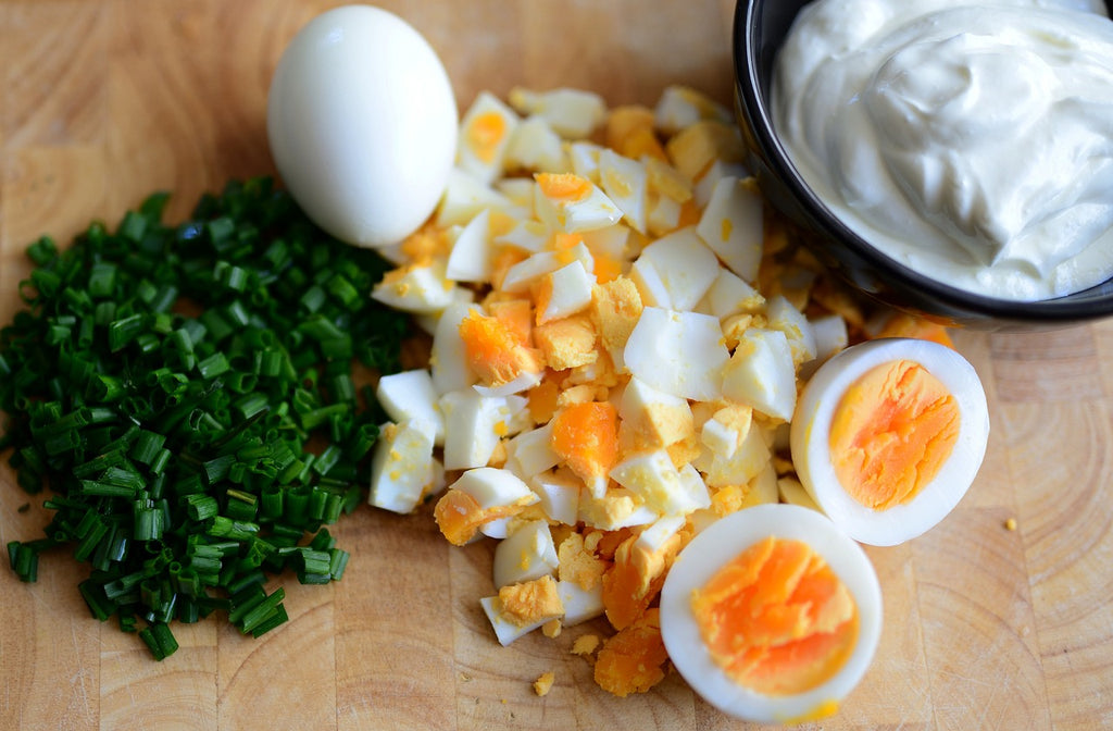 Boiled eggs chopped and cut in halves with a bowl of mayonnaise and spring onions on the side.