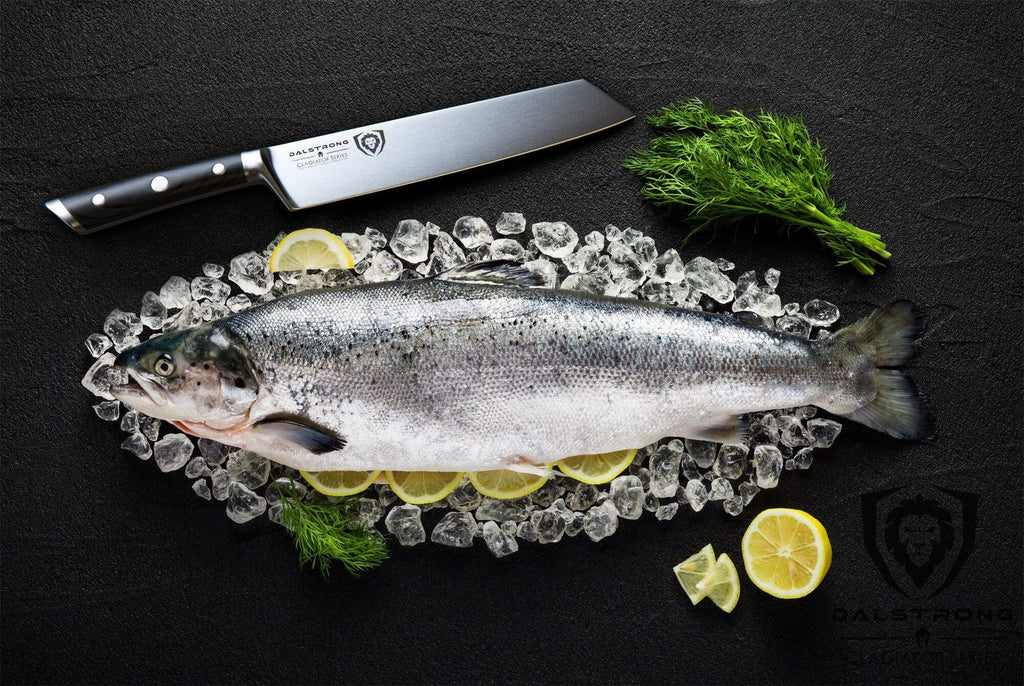 Large uncooked fish against a black surface next to a sharp kiritsuke knife