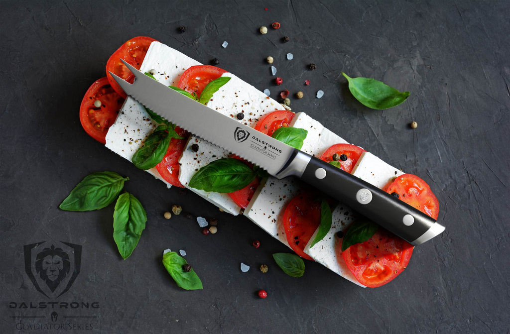 A serrated knife balancing on a bed of cheese and sliced tomatoes against a black backdrop
