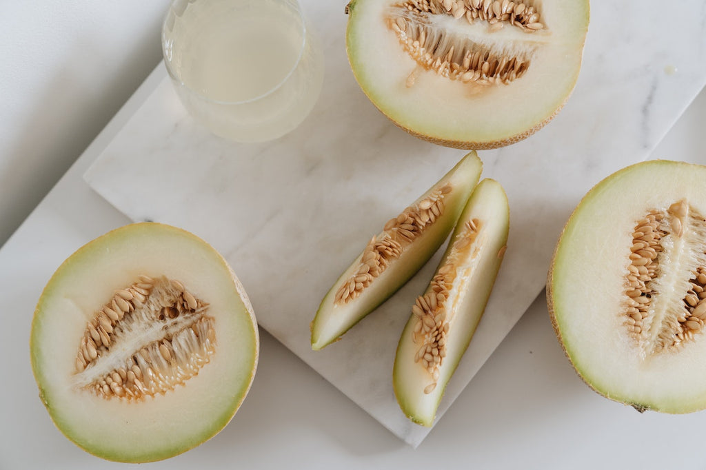 Different slices of fresh melon beside a glass on a marble counter.