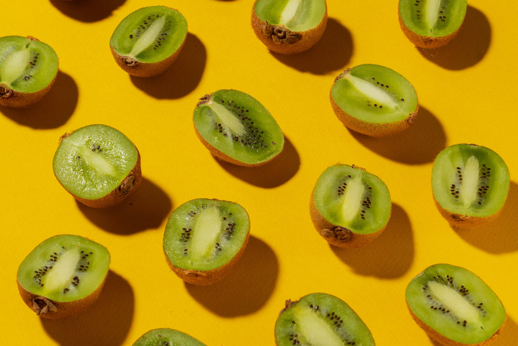 Fourteen slices of fresh kiwi on a yellow surface