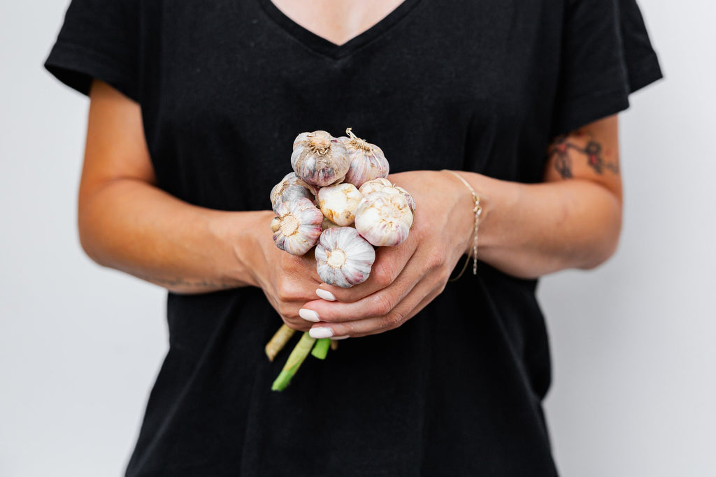 Photo of a person in a black shirt holding a bunch of garlic bulbs in a white background