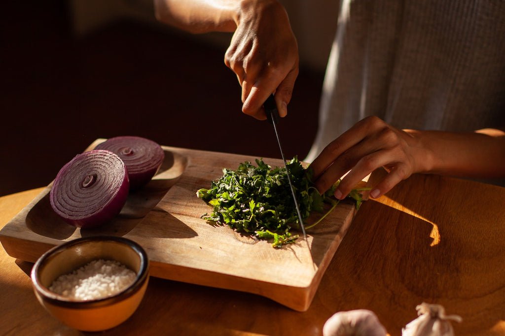 A close-up photo of a person cutting a cilantro on a wooden cutting board