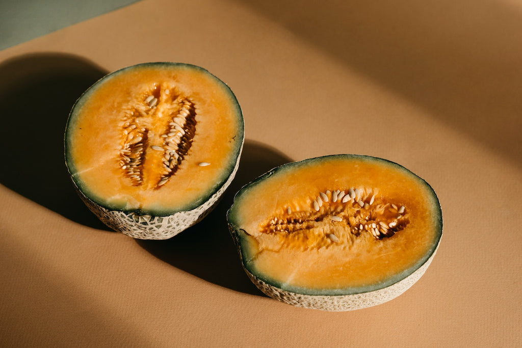 Raw fresh melon sliced in half on a flat orange table.
