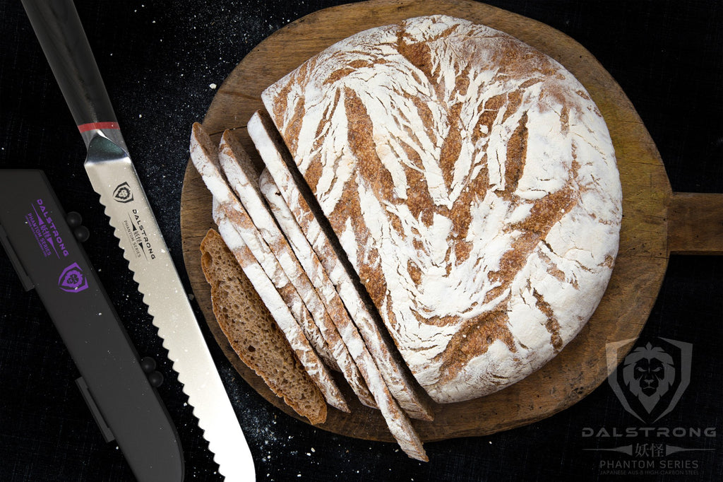 Circular loaf of bread on a cutting board next to a bread knife on a dark surface