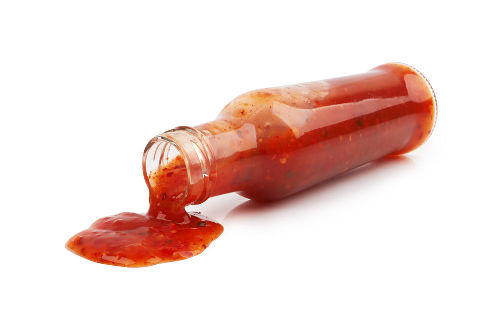 An overturned glass bottle of red hot sauce pouring onto a white surface