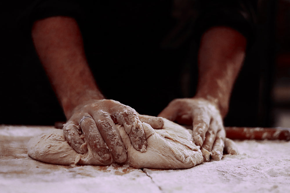 Man with sleeves rolled up kneading dough on a hard surface