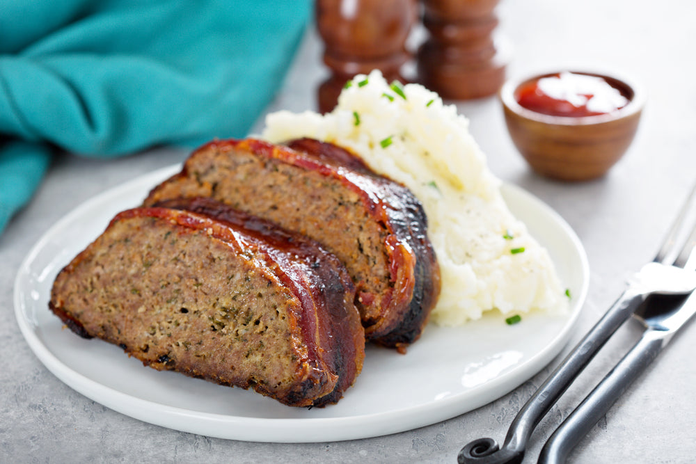 Two slices of meatloaf on a white plate with mashed potato