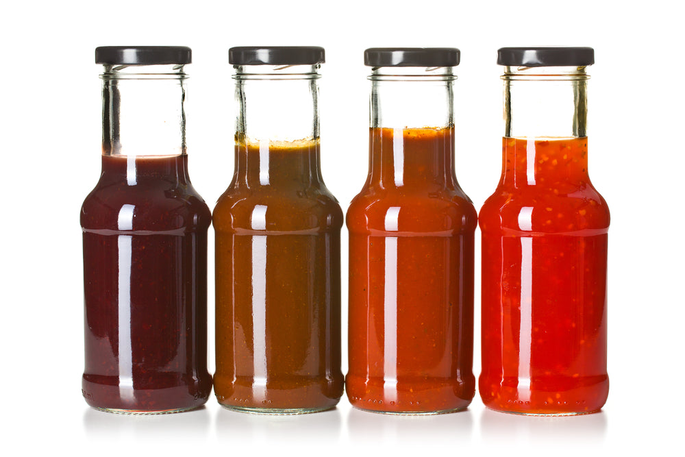 Four glass jars filled with different colored bbq sauces