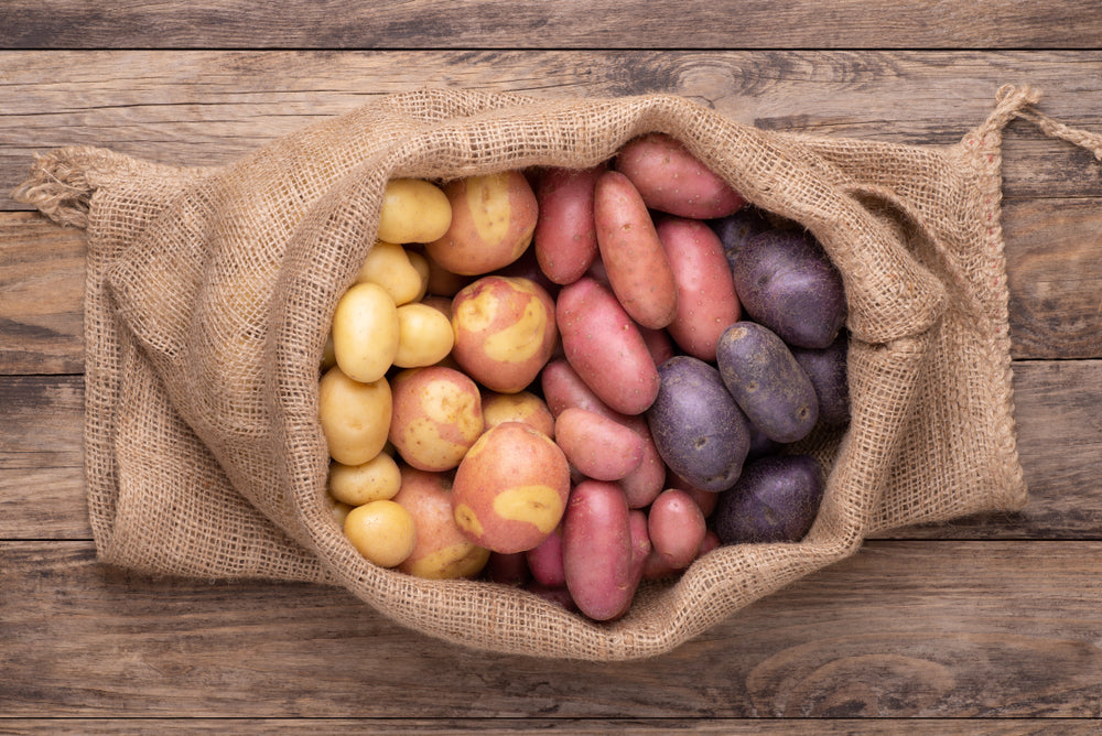 A sack filled with different coloured potatoes on a wooden surface
