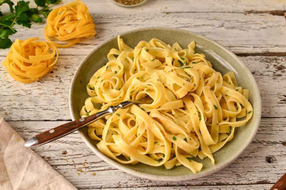 Italian pasta in a plate with a fork. Fettuccini pasta with cheese, cream, parsley, on a light background.