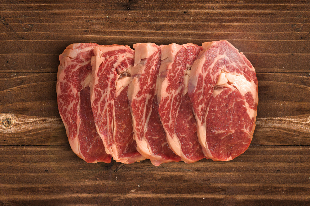 Five pieces of raw rib eye steaks on a wooden surface