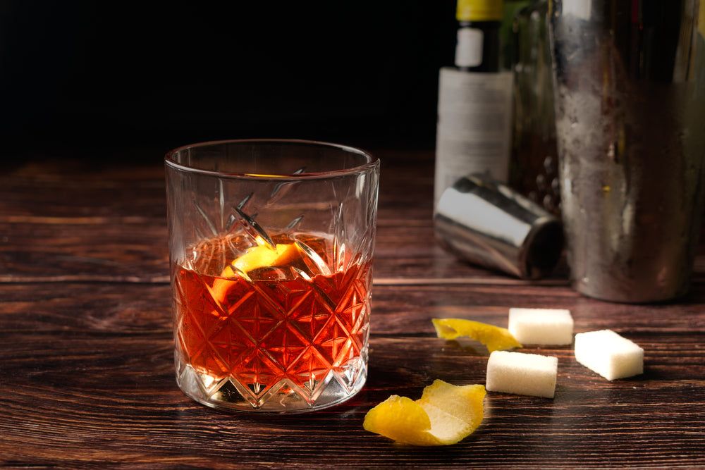 Sazerac cocktail in a old fashioned glass, with a lemon peel, on a dark wooden background.