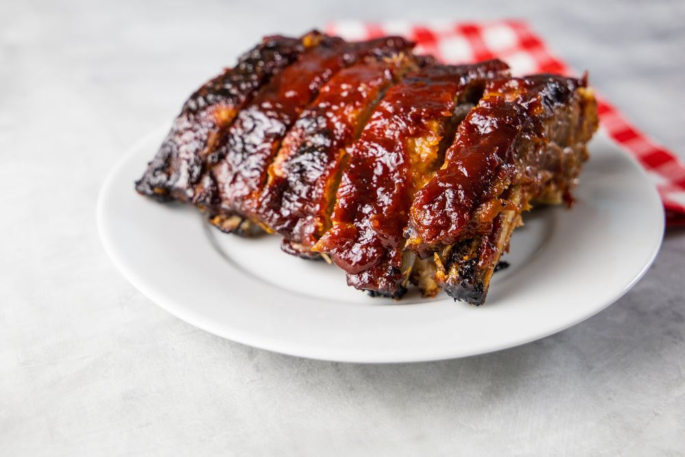 A white plate of bbq ribs marinated in sauce
