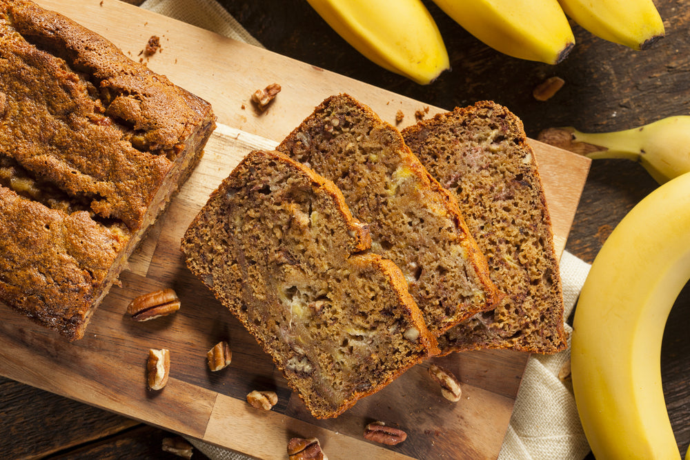 Three slices of banana bread cut from the load on a chopping board next to four bananas