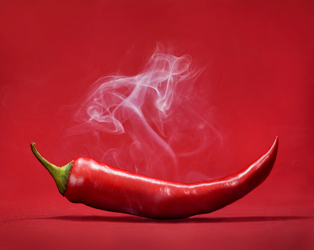 A spicy red pepper against a red background with smoke coming from it