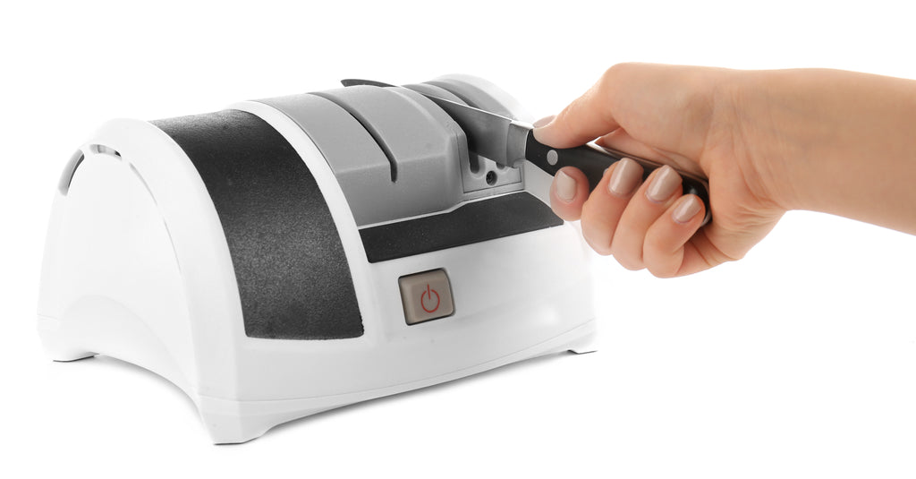 A person's right hand places a knife into a white and grey electric knife sharpener on a white background