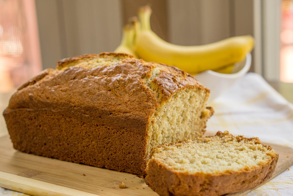 Banana Bread Loaf on a cutting board with bananas in the background