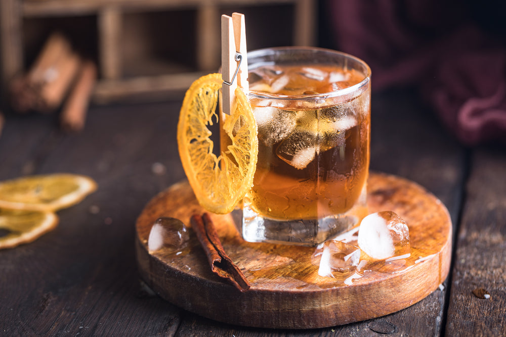 Cocktail with iced tea, whiskey, orange and ice in a glass on the wooden tray on the dark background