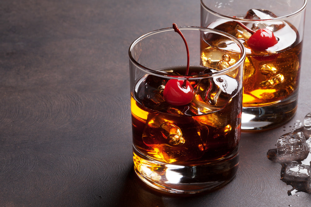 Manhattan cocktail with whiskey in two glasses with a cherry in each one against a dark surface