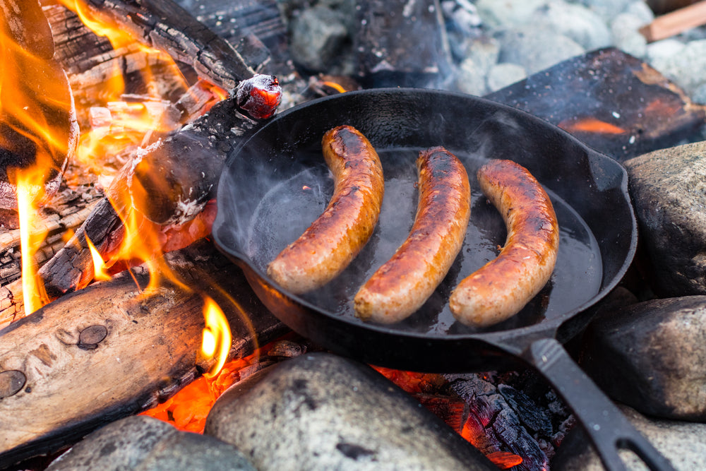 Live fire cooking juicy sausages over campfire.