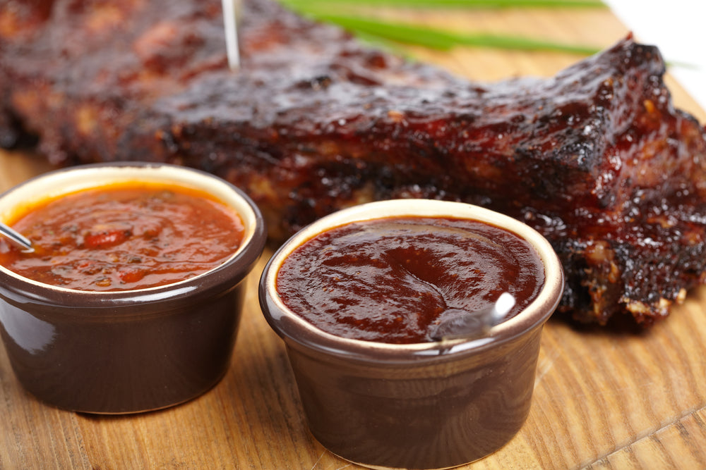 BBQ Ribs on a cutting board next to two small containers of different colored sauces