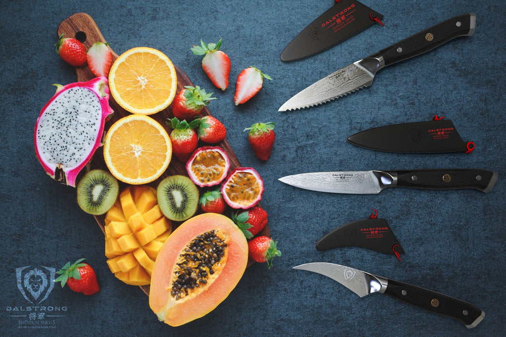 Three small paring knives on a blue surface facing several sliced fruits